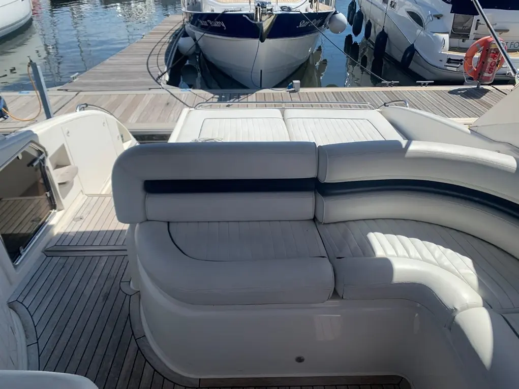 Luxury motorboat featuring white leather seating and wooden decking, moored at a marina with other vessels nearby.
